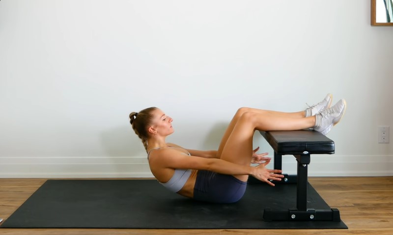 Devojka radi trbušnjake u stanu uz pomoć klupe za vežbanje